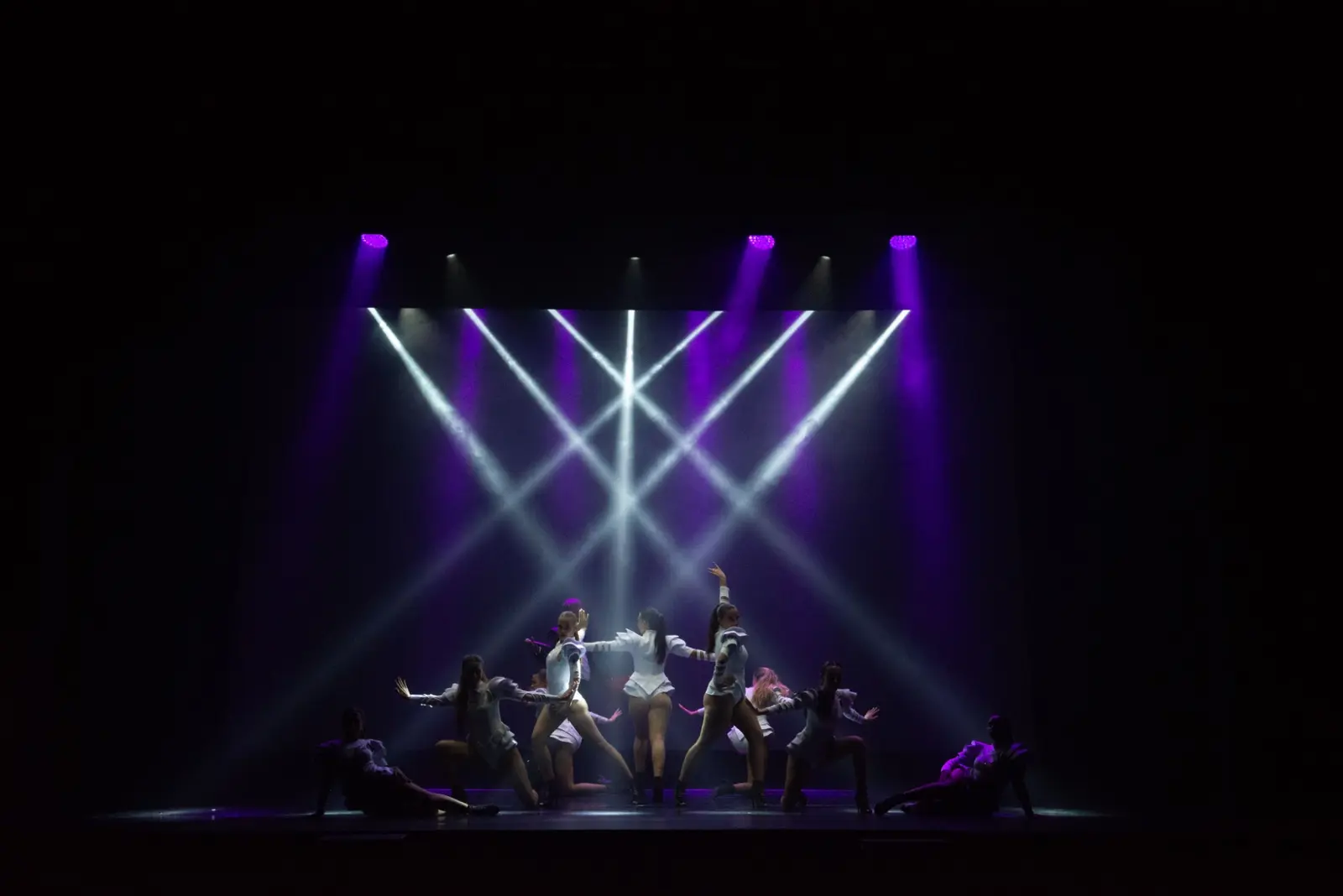 Corpo di ballo in bianco sotto fasci di luce viola